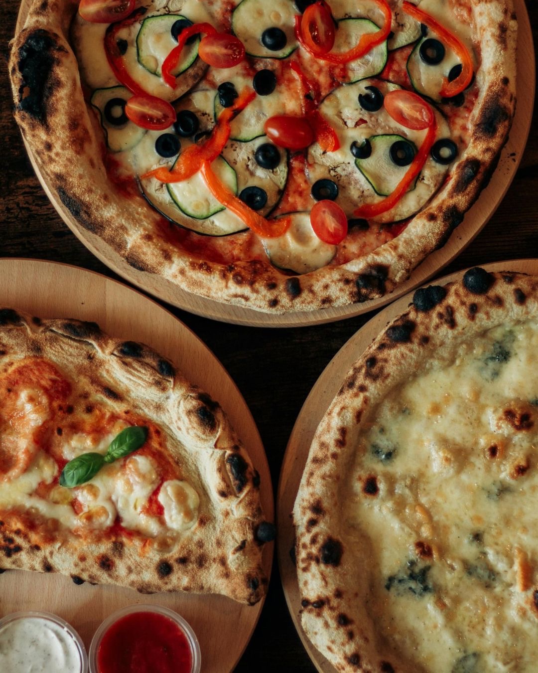 A spread of three pizzas and a calzone with dips