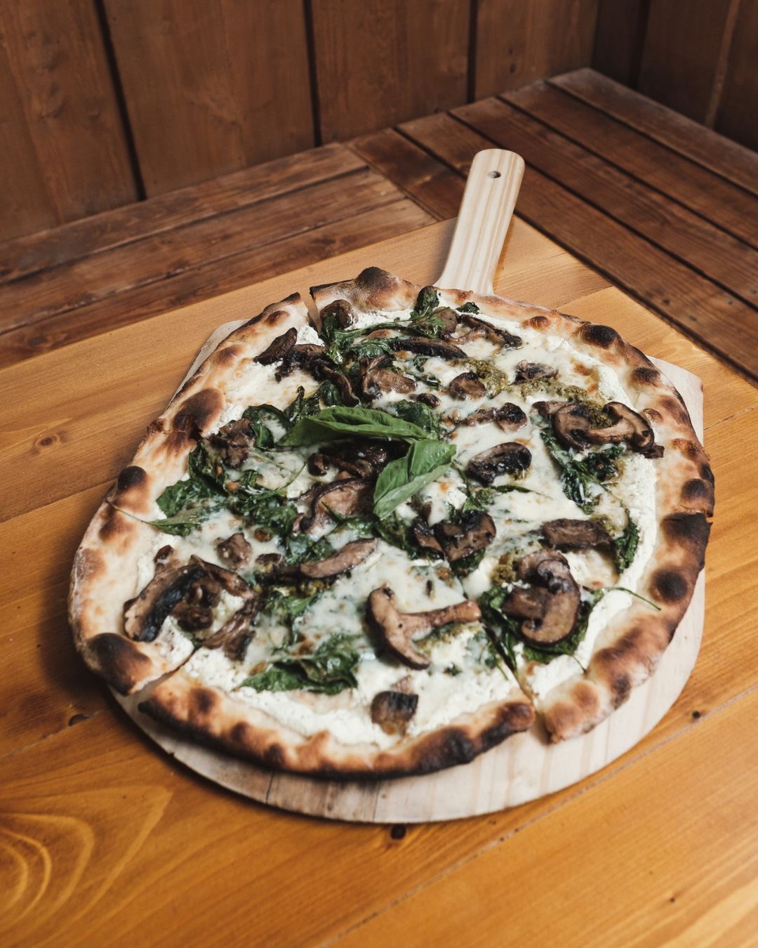 White pizza with mushrooms and spinach on a wooden peel